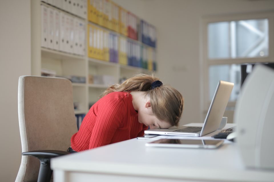 A woman rests her forehead on her laptop.